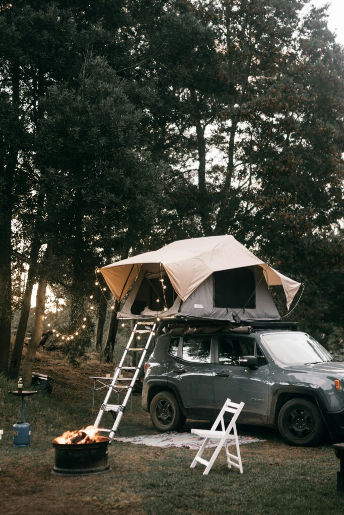 Cozy campsite with car rooftop tent and campfire under trees at dusk.